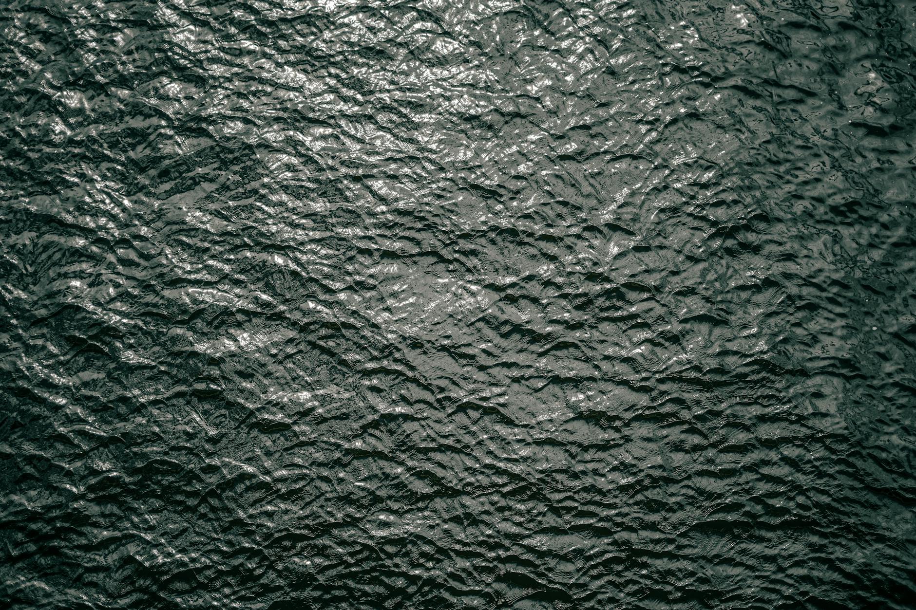 Close-up texture of calm dark green water with gentle ripples, evoking the still, weightless quality of a float session