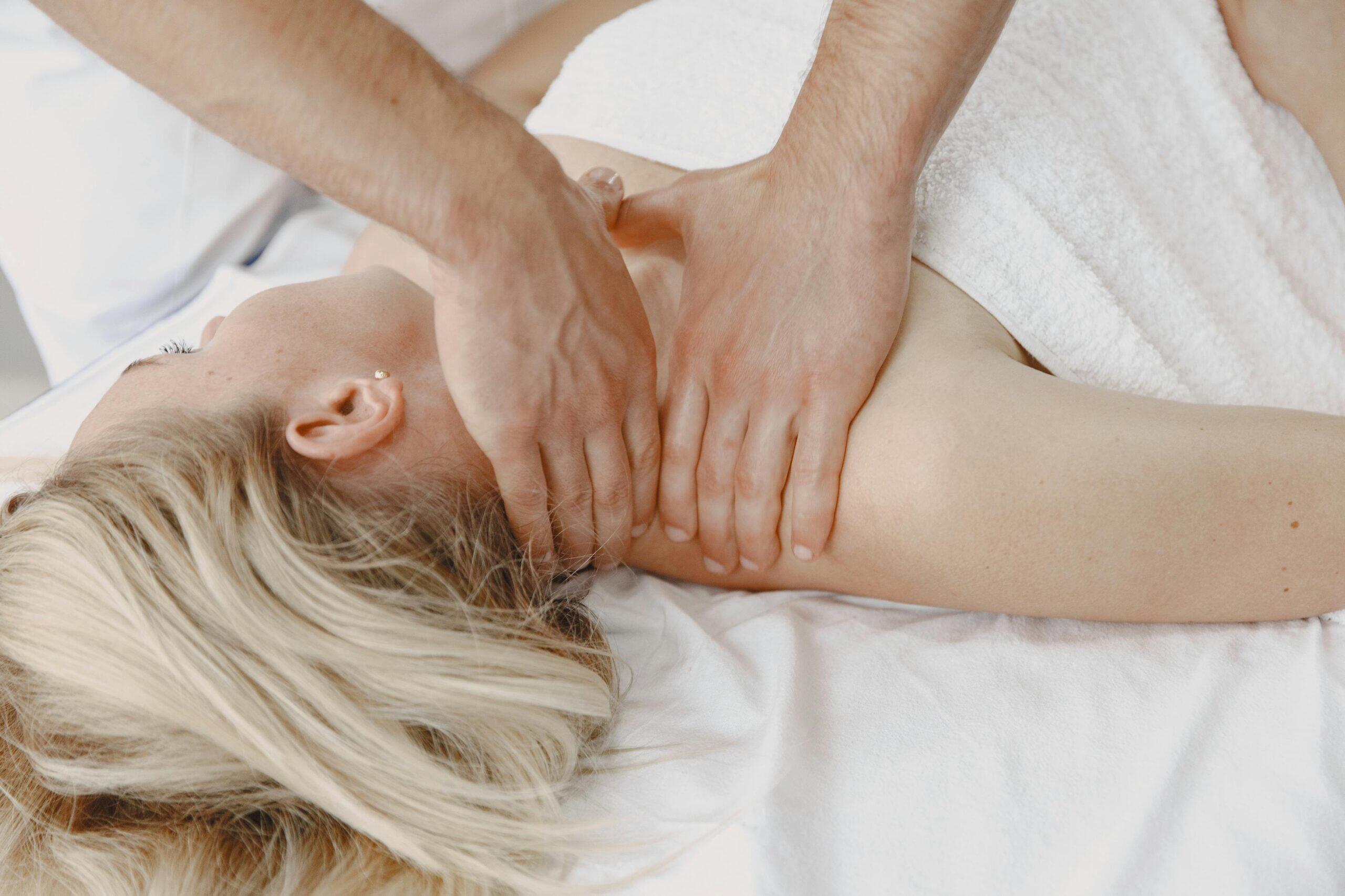 A massage therapist works on a woman's neck and shoulder area in a calm, well-lit spa setting, demonstrating professional technique
